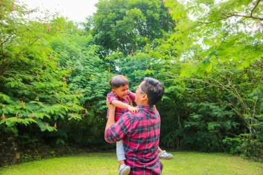 Baba oğlunu bahçede havaya kaldırıyor.