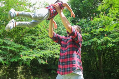 Asyalı baba parkta oynarken oğlunu havaya kaldırıyor.