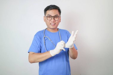 Koruyucu PPE takımlı Asyalı doktor, beyaz arka planda izole edilmiş enfeksiyonu korumak için mavi eldiven takıyor..