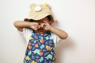 Asyalı çocuk ağlayarak gözyaşlarını parmaklarıyla silerken duygusal kargaşa başlıyor. Beyaz arka planda izole edilmiş, anaokulu çocuğu ifade eden yüz hüzün ve hüsranın canlı bir resmini çizer.