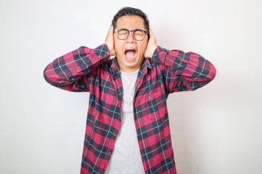 Asyalı asyalı asyalı sinirli bir adam. Elleriyle kulaklarını kapatıyor. Beyaz arka plandaki gürültüden rahatsız oluyor.