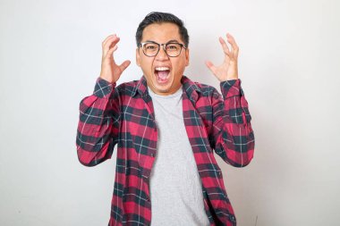 Şok olmuş ve paniğe kapılmış Asyalı bir adam kötü habere tepki veriyor, beyaz arka planda panik içinde duruyor ve kararsız bir şekilde el sıkışıyor, ne yaptığını bilmiyor, kendini işe yaramaz, beyaz arka planda hissediyor.