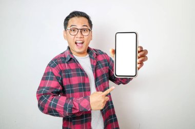 Mutlu yakışıklı Asyalı adam mavi arka planda izole edilmiş boş ekran akıllı telefon modeli gösteriyor..