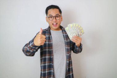 Asyalı işadamı gülümsüyor ve elinde para tutarken başparmağını bırakıyor.