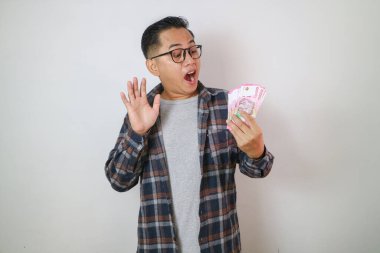 Heyecanlı genç yakışıklı Asyalı adam elinde bir deste para tutuyor beyaz arka planda izole edilmiş.