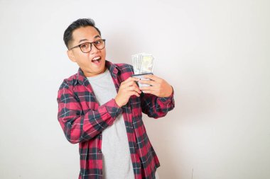 Ekose gömlekli genç Asyalı bir adamın portresi. Elinde Rupiah banknotlarıyla dolu bir cüzdan var. Beyaz arka planda izole edilmiş. insanlar yaşam tarzı konsepti