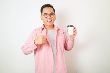 Elinde kağıt kahve fincanı tutan gülümseyen Asyalı genç bir adamın portresi beyaz arka planda izole edilmiş hareket işareti gösteriyor.