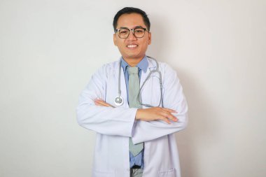 Beyaz önlüklü, kendinden emin, yakışıklı, orta yaşlı Asyalı erkek terapist, steteskoplu gözlükler beyaz arka planda izole edilmiş kameraya bakıyor. Hastalık tedavisi, sağlık, ilaç, teklif ve reklam