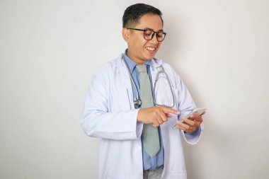 Asyalı erkek doktor, hastanede dokunmatik ekranı olan modern bir akıllı telefon cihazı kullanarak mavi bir gömlek giyiyor. Sağlık ve Tıp Konsepti.