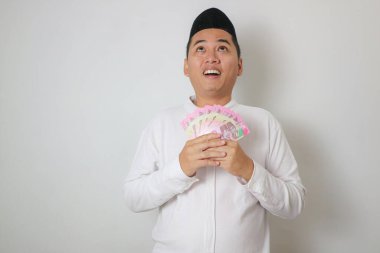 Müslüman Asyalı adam elinde kağıt para tutarken mutlu gülümsüyor.