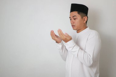 Asyalı Müslüman adam avucunu önde gösteriyor, beyaz arka planda izole edilmiş bir şey tutuyor.