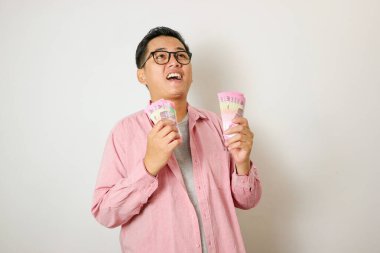 Heyecanlı genç yakışıklı Asyalı adam elinde bir deste para tutuyor beyaz arka planda izole edilmiş.