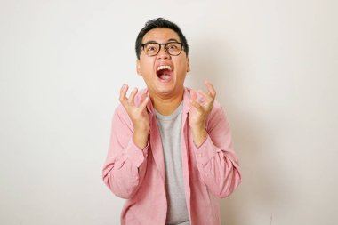 Şok olmuş ve paniğe kapılmış Asyalı bir adam kötü habere tepki veriyor, beyaz arka planda panik içinde duruyor ve kararsız bir şekilde el sıkışıyor, ne yaptığını bilmiyor, kendini işe yaramaz, beyaz arka planda hissediyor.