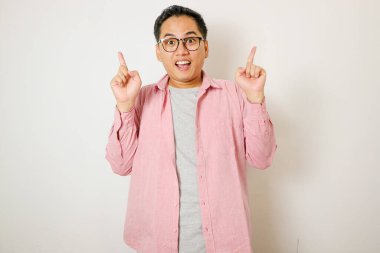 Happy handsome smiling young Asian man with hands poiting up to empty space above