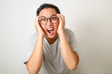 İnsanlar, İnsan Duyguları ve Duyguları Konsepti. Şaşırmış, korkmuş, ağzı açık, yüzüne dokunan ve beyaz stüdyo duvarında izole bir şekilde kameraya bakan Asyalı adamın portresi.