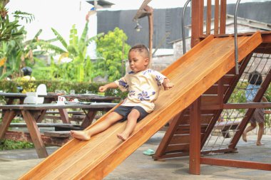 Asyalı çocuk kaygan bar oyuncağında oynarken gülümsüyor açık hava oyun parkında, mutlu anaokulu çocuğu yazın oyun parkında oynarken eğleniyor, küçük çocuk tırmanıyor.