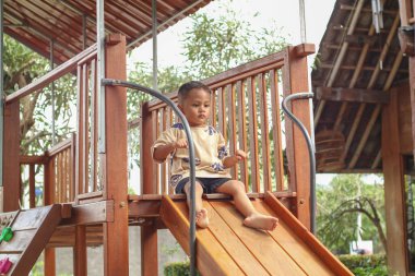 Küçük tatlı Asyalı, 2 yaşında, küçük bir çocuk. Alışveriş merkezinin kapalı alanındaki çocuk parkında kaydırağında oynuyor. Bebek Kayıyor, Çocuk ilk deneyim konsepti..