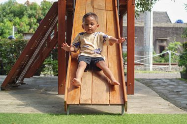 Çocuk dışarıda oyun oynuyordu. Çocuklar okulda ya da anaokulunda oynarlar. Aktif çocuk renkli kayıyor ve sallanıyor. Çocuklar için sağlıklı bir yaz aktivitesi. Küçük çocuk dışarı tırmanıyor..