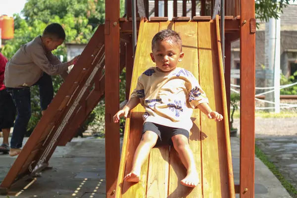Şirin 3 yaşındaki çocuk serin bulutlu bir günde sarı bir oyun parkında heyecanlı bir şekilde oynuyor.