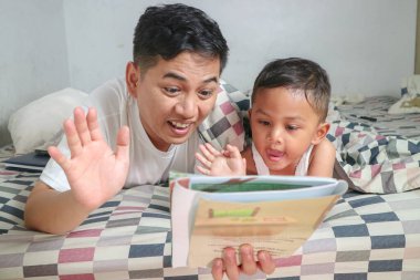 Baba ve sevimli küçük Asyalı çocuk 3 yaşında çocuk, uyku zamanı masal kitabı okuyor, evde yatakta yatıyor, baba ve oğul birlikte kaliteli zaman geçiriyor, ebeveynler çocuk konseptine kitap okuyor.