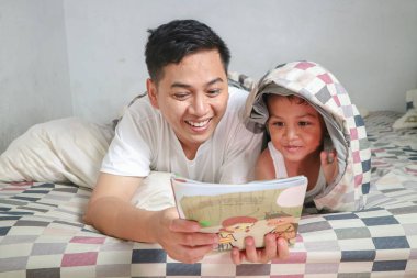 Baba ve oğul yatakta, birlikte kitap okuma