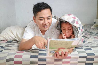 Genç baba ve küçük oğlu evde birlikte kitap okuyorlar.