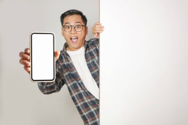 Beyaz bir duvarın arkasından gözetleyen Asyalı bir adam beyaz bir ekranla elinde akıllı bir telefonla heyecan ve şok yaratıyor. Beyaz bir arkaplanda izole edilmiş