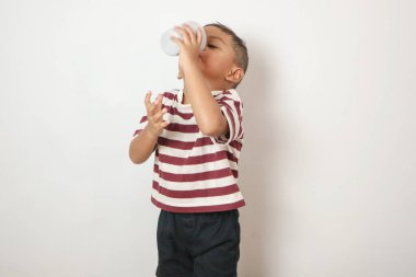 Beyaz tişörtlü Asyalı genç çocuk elinde bir bardak taze su tutuyor ve içiyor. Su gününü kavra.