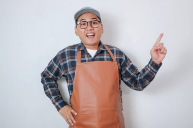 Genç, şaşkın Hintli garson önlüklü, beyaz izole edilmiş arka planda fotokopi alanını işaret ediyor, üniformalı Hintli barista erkek, hayret içinde reklamını yapıyor.