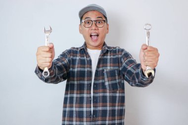 Hintli mutlu otomobil tamircisi mavi takım elbise ve şapka tutucu anahtar ile dizüstü veya kontrol listesi veya yazı defteri veya akıllı telefon kullanarak