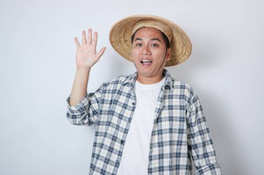 Asyalı çiftçi kendine güvenerek gülümserken elini kaldırıyor ve selam veriyor.