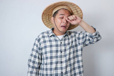 Yorgun ve stresli Asyalı çiftçi başını tutarken ayakta duruyor. Beyaz arkaplanda izole