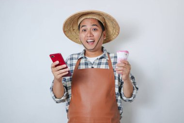 Endonezyalı genç çiftçi elinde tuttuğu akıllı telefon ve parayla mutlu bir şekilde gülümsüyor.