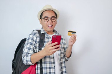 Yakışıklı ve neşeli genç Asyalı erkek turist elinde akıllı telefon ve kredi kartıyla güzel tapınağı ziyaret ederken mobil bankacılık uygulamasını kullanıyor..