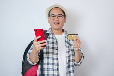 Kredi kartı ve akıllı telefon tutan neşeli Asyalı bir adam. Sıradan bir tişört giymiş. Beyaz arkaplanlı stüdyoyu kapat.