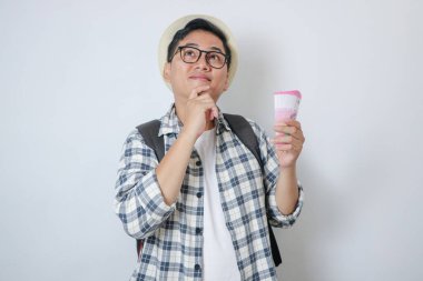 Genç Asyalı gezgin, Endonezya 'nın kağıt parasıyla düşünürken jest yapıyor.