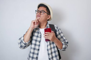 Cep telefonu tutarken bir şey düşünen Asyalı bir sırt çantalı.