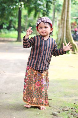 Geleneksel Cava kıyafetleri giyen Asyalı çocuk kibarca poz veriyor ve beyaz arka planda izole edilmiş bir şekilde selamlıyor. Batik Lurik giyen çocuk.