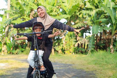 Gülümseyen mutlu aile, güneşli bir günde Avrupa sokaklarında bisiklet sürmekten hoşlanıyor. Parkta bisikletle gezen çocuklu bir anne. Güvenli bebek sandalyesinde oturan çocuk. Sağlıklı yaşam tarzı aktiviteleri
