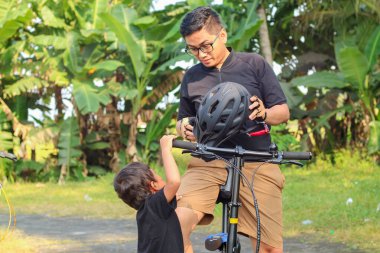 Baba oğul parkta bisiklete biniyorlar.