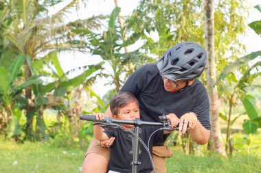 Baba ve oğlunun yolda bisiklet sürerken çekilmiş bir fotoğrafı.
