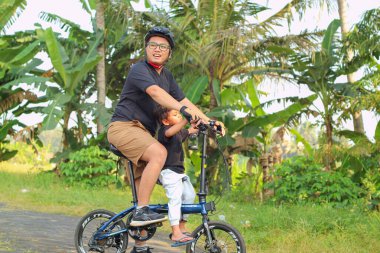 Oğlu bisikletle gezen mutlu Asyalı baba. Aile, park konseptinde birlikte hareket eder.