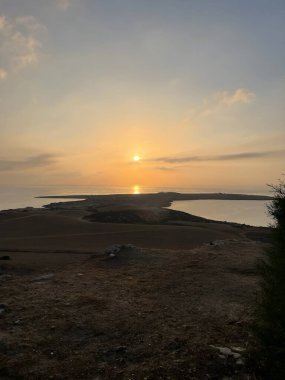 The serene sunset bathes Cape Greco in golden light, highlighting the untouched coastal terrain of Famagusta, Cyprus. The tranquil sea mirrors the warm sky tones. clipart