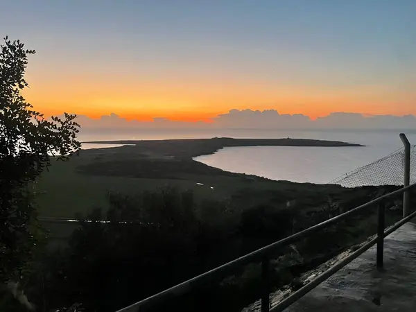 Kıbrıs, Cape Greco 'da sakin bir günbatımı, gökyüzünü gölgeli bulutlarla altın renklerde boyuyor. Sakin deniz ve doğal manzara huzurlu bir kıyı manzarası yaratır..