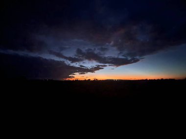 A mesmerizing twilight sky over Avgorou, Cyprus, with dramatic clouds and glowing orange horizons. The scene captures the mysterious beauty of the countryside at dusk. clipart