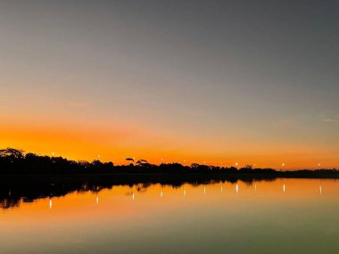 Gün batımı ve şehir ışıklarıyla aydınlanan büyük bir göl. 