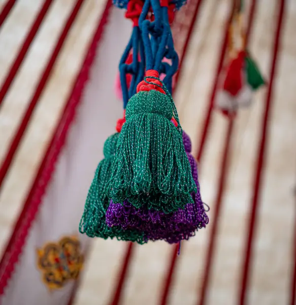 Fotoğrafta yeşil bir kabloda asılı duran parlak el yapımı yün ponpon kızlar görülüyor. Geleneksel yurtta dekoratif unsurlar olarak kullanılıyorlar..