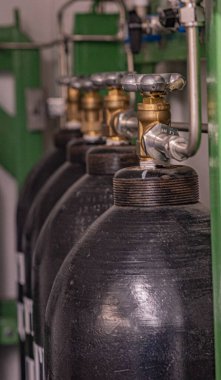 Fotoğraf, boru ve vanalardan oluşan bir sisteme bağlı siyah metal sıkıştırılmış hava silindirlerini gösteriyor. Silindirler 