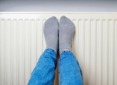 Warming Feet on White Radiator, Man Warms his Feet at Home, Cold Winter, Expensive Electricity Saving Concept, Copy Space