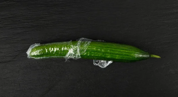 Plastic Wrapped Cucumber, Vegetable in Film Packaging, Film Wrap Food, Eat Plastic Concept, Black Background